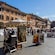 Art vendors displaying paintings under sun umbrellas in an Italian plaza surrounded by buildings